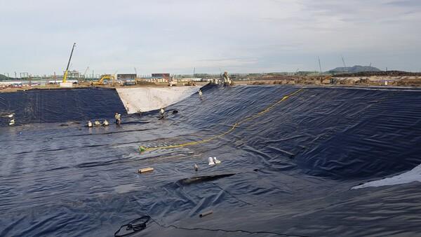 Tấm màng HDPE dày 0.5mm đang được trải trên đáy hồ chứa nước thải công nghiệp, tạo thành một lớp lót chống thấm hiệu quả, ngăn chặn ô nhiễm nguồn nước ngầm.